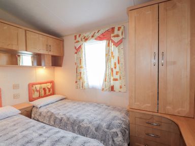 A bedroom with two single beds a window with patterned curtains and wooden cabinets at The Cabin in Occumster near Lybster