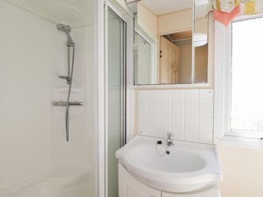 A bathroom with a shower area, a sink with a cabinet, a mirror, and a window at The Cabin in Occumster near Lybster