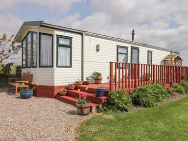 A mobile home with a red wooden deck and flower pots on and around the steps at The Cabin in Occumster near Lybster