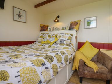 A bedroom with a bed, chair, and wall art at The Journeyman Luxury Shepherds Hut in Barnoldswick