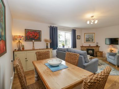 A dining area with a wooden table and woven chairs next to a living room with a gray sofa a fireplace and a wall-mounted TV at Phocle Ridge in Phocle Green near Ross-On-Wye