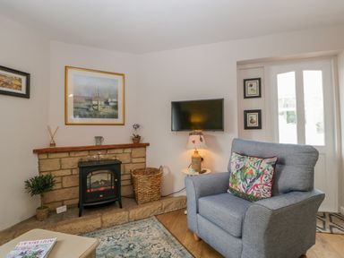 A living room with a grey armchair a fireplace and a wall-mounted television at Phocle Ridge in Phocle Green near Ross-On-Wye