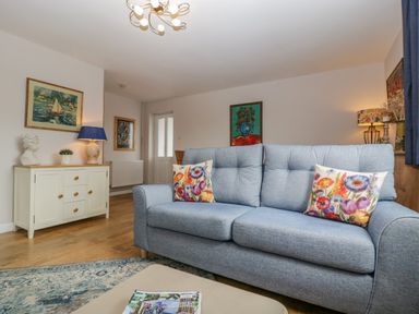 A living room with a blue sofa with floral cushions a sideboard with a lamp and sculpture and paintings on walls at Phocle Ridge Phocle Green near Ross-On-Wye