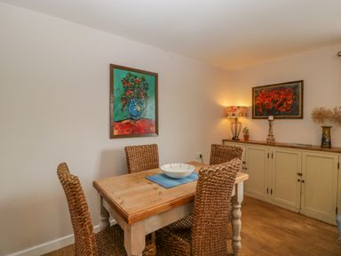 A dining area with a wooden table and four wicker chairs with paintings on the walls at Phocle Ridge in Phocle Green near Ross-On-Wye