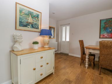 A dining area with a wooden table and wicker chairs beside a cabinet with a lamp plant and bust at Phocle Ridge in Phocle Green near Ross-On-Wye