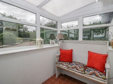 A white bench with cushions and pillows next to windows in a sunroom at Phocle Ridge in Phocle Green near Ross-On-Wye