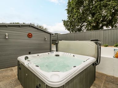 An outdoor hot tub with water on a tiled patio next to a grey wooden shed and fenced garden at Phocle Ridge in Phocle Green near Ross-On-Wye