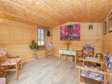 A room with wooden walls and ceiling with four wooden chairs with floral cushions a white table with two boxes under it and a colorful painting on the wall at Phocle Ridge in Phocle Green near Ross-On-Wye
