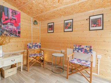 A small wooden room with two floral patterned chairs a round side table a white desk a wooden crate and framed artwork on the walls at Phocle Ridge in Phocle Green near Ross-On-Wye
