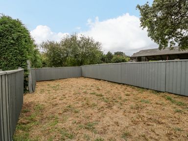 A fenced backyard with dry grass and surrounding trees at Phocle Ridge in Phocle Green near Ross-On-Wye