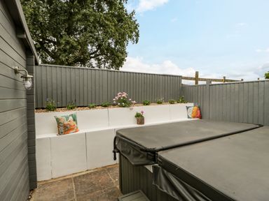 An outdoor patio area with a hot tub a white built-in bench with cushions and plants behind a grey wooden fence at Phocle Ridge in Phocle Green near Ross-On-Wye