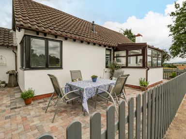 An outdoor patio area with a table covered by a patterned tablecloth and four chairs beside a house at Phocle Ridge in Phocle Green near Ross-On-Wye