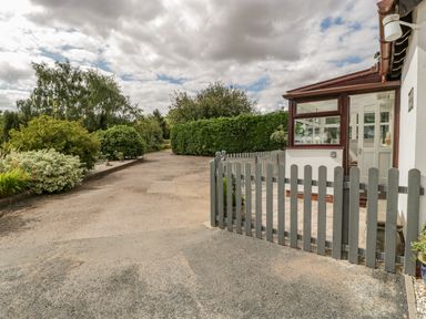 A driveway with bushes and trees next to a small fenced porch at Phocle Ridge in Phocle Green near Ross-On-Wye