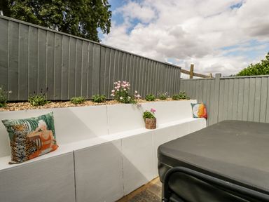 An outdoor seating area with white built-in benches cushions and flower pots by a grey wooden fence at Phocle Ridge in Phocle Green near Ross-On-Wye