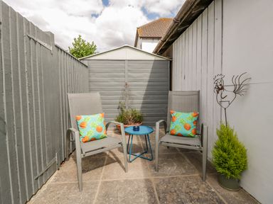 An outdoor patio area with two chairs with pineapple cushions a small blue table a potted plant and a garden shed at Phocle Ridge in Phocle Green near Ross-On-Wye