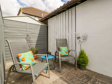 A small outdoor patio with two chairs with pineapple pillows a small blue side table and a potted plant at Phocle Ridge in Phocle Green near Ross-On-Wye