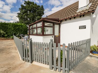 A white house with a brown roof and a glass porch behind a grey picket fence at Phocle Ridge in Phocle Green near Ross-On-Wye