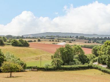 A rural landscape with fields trees and hills under a cloudy sky at Phocle Ridge in Phocle Green near Ross-On-Wye