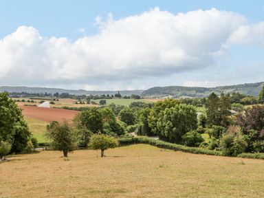 A rural landscape with trees fields and hills under a cloudy sky at Phocle Ridge in Phocle Green near Ross-On-Wye
