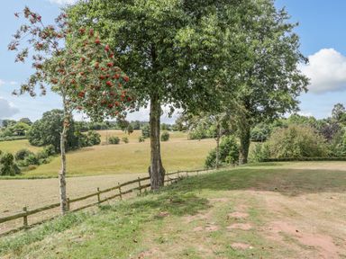 A grassy area with trees and a wooden fence overlooking fields at Phocle Ridge in Phocle Green near Ross-On-Wye