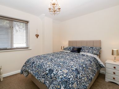 A bedroom with a bed with floral bedding a window with blinds and a bedside table with lamps at Phocle Ridge in Phocle Green near Ross-On-Wye