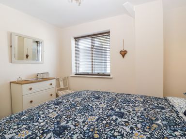 A bedroom with a floral patterned bedspread a white dresser a chair a window with blinds and a wall mirror at Phocle Ridge in Phocle Green near Ross-On-Wye