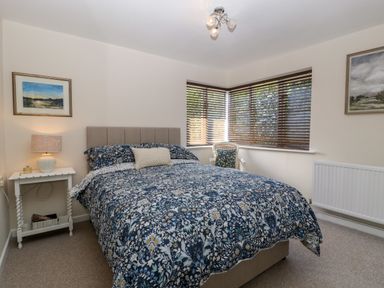 A bedroom with a patterned bedspread a bedside table and a chair near windows at Phocle Ridge in Phocle Green near Ross-On-Wye