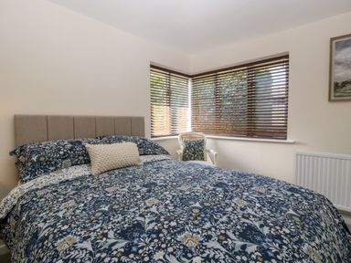 A bedroom with a bed covered in floral patterned bedding next to a corner window with blinds and a chair at Phocle Ridge in Phocle Green near Ross-On-Wye