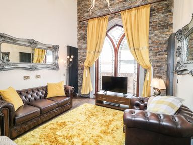 A living room with brown leather sofas yellow cushions a yellow rug and a TV in front of arched windows at The Upper Room in Ballymena