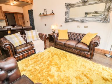 A living room with brown leather sofas yellow cushions and a yellow rug at The Upper Room in Ballymena