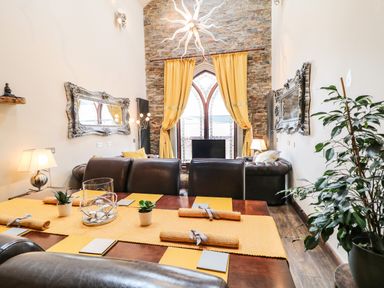 A dining area with a wooden table and brown leather chairs next to a living room with brown leather sofas and yellow curtains in front of a window at The Upper Room in Ballymena