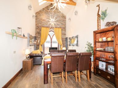 A dining area with brown chairs and a wooden table next to a living room with yellow curtains and a leather sofa at The Upper Room in Ballymena