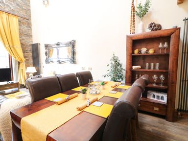 A dining room with a wooden table set with yellow placemats and rolled napkins at The Upper Room in Ballymena