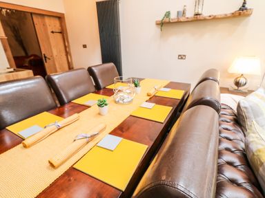 A dining table set with yellow placemats and napkins with brown leather chairs and a brown leather bench at The Upper Room in Ballymena