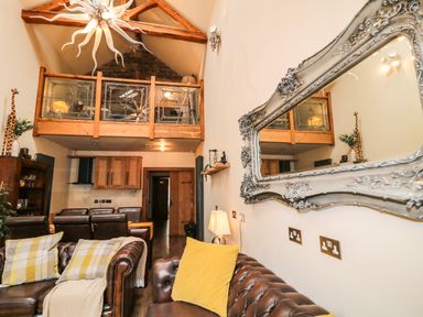 A living room with leather sofas yellow pillows wooden kitchen cabinets and a balcony with glass railing at The Upper Room in Ballymena