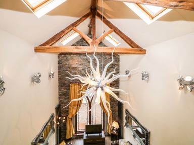 A living room with exposed wooden beams skylights chandelier and stone wall with arched window at The Upper Room in Ballymena