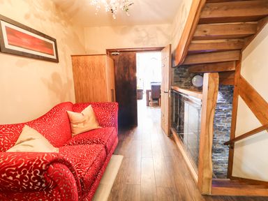 A hallway with a red patterned sofa beige cushions wooden wardrobe wooden stairs and a door leading to another room at The Upper Room in Ballymena