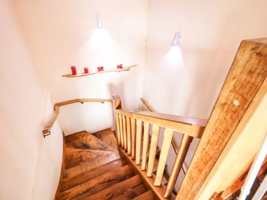 A wooden staircase with wall lights and red candles on a floating shelf at The Upper Room in Ballymena