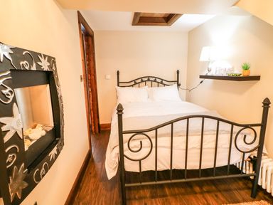 A bedroom with a black metal bed frame white bedding a wall-mounted lamp and shelf and a decorative fireplace at The Upper Room in Ballymena
