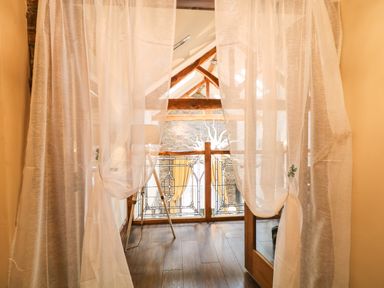 A wooden balcony railing with decorative glass panels and an easel behind sheer white curtains at The Upper Room in Ballymena
