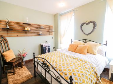 A bedroom with a bed, heart-shaped mirror, wooden chair, shelves with decor at The Upper Room in Ballymena