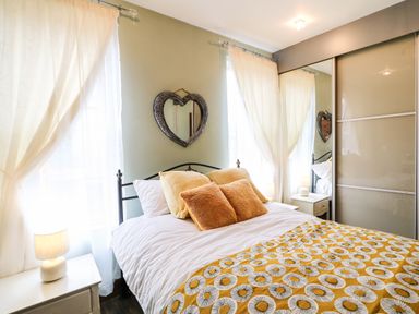 A bedroom with a double bed with yellow and brown pillows and a patterned blanket next to nightstands with lamps and a heart shaped mirror on the wall at The Upper Room in Ballymena