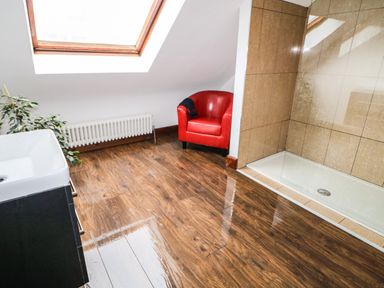 A bathroom with wooden floor tiles a red armchair a glass shower enclosure a sink and a skylight window at The Upper Room in Ballymena