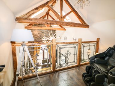 A loft area with wooden beams stained glass railing a floor lamp and a black massage chair at The Upper Room in Ballymena