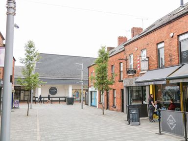 A pedestrian street with trees and shops including a coffee shop and hair salon at The Upper Room in Ballymena