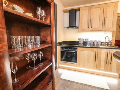 A kitchen with wooden cabinets a black countertop a built-in oven a kettle and glassware on wooden shelves at The Upper Room in Ballymena