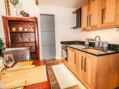 A kitchen with wooden cabinets and black countertop next to a dining table with yellow placemats at The Upper Room in Ballymena