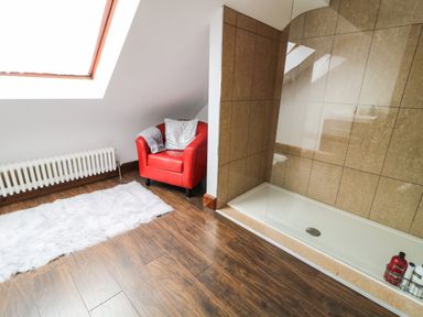 A bathroom with a walk-in shower, a red armchair, a white rug, and a radiator at The Upper Room in Ballymena