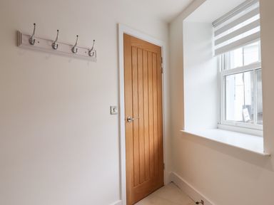 A wall with five metal hooks a wooden door and a window with striped blinds at Ferryside in Kingswear