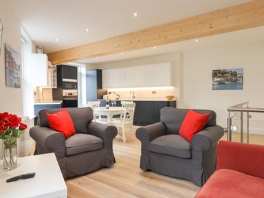 A living room with two gray armchairs with red cushions and an open kitchen with black and white cabinets at Ferryside in Kingswear